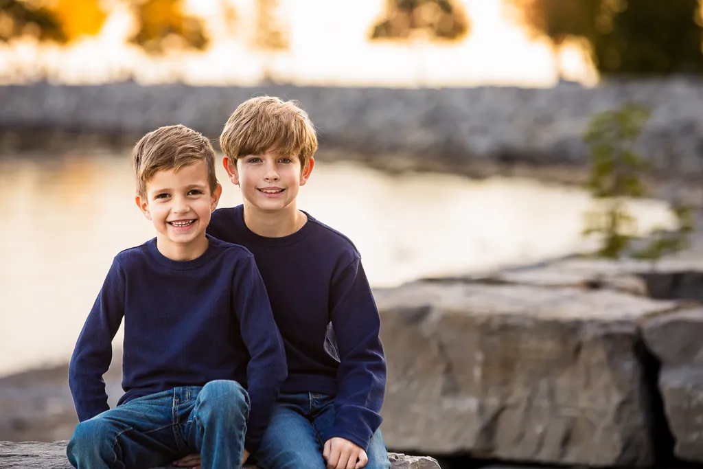 Two young brothers sitting on shoreline rocks during Toronto fall family photography session