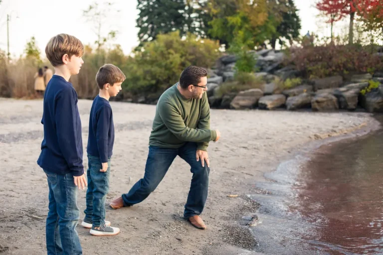 Father and sons skipping stones together at the beach during a candid fall family session at Scarborough Bluffs