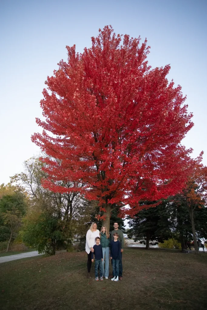 Family standing under a vibrant red maple tree during a fall photo session at Scarborough Bluffs