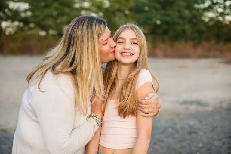 Candid moment of mother kissing her daughter's cheek on the beach at sunset during a fall family session at Scarborough Bluffs