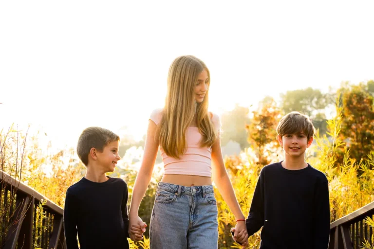 Three siblings holding hands and walking together at Scarborough Bluffs during a sunlit fall family photo session