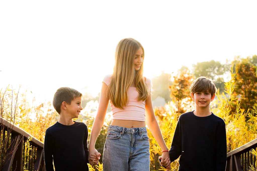 Three siblings holding hands and walking together at Scarborough Bluffs during a sunlit fall family photo session