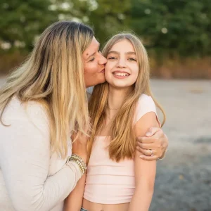 Candid moment of mother kissing her daughter's cheek on the beach at sunset during a fall family session at Scarborough Bluffs
